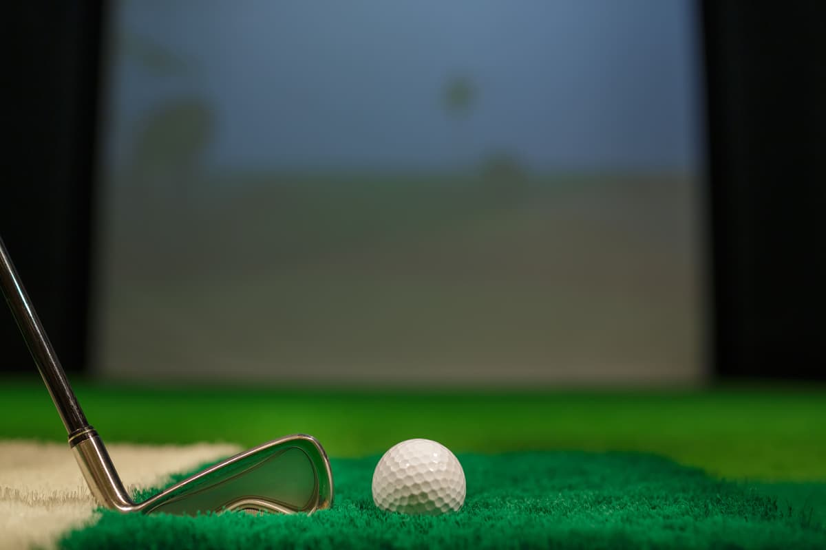 Golf ball and club on turf in front of a simulator screen